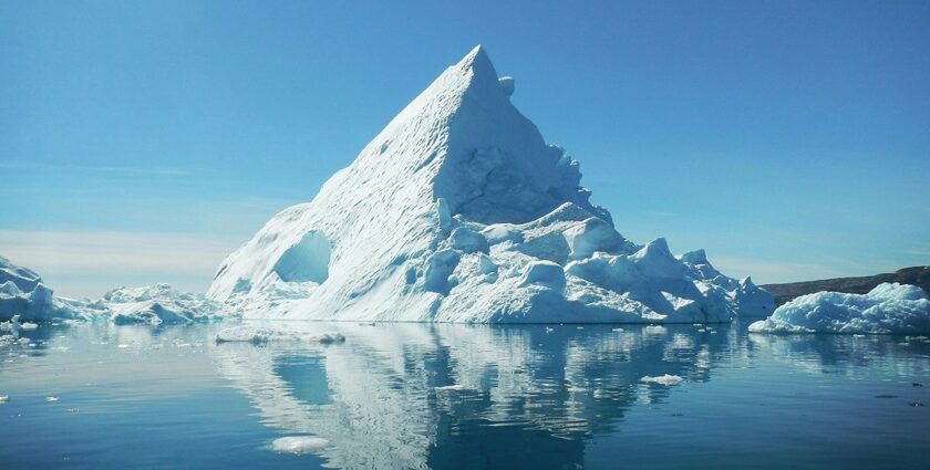 A clear reflection of a massive iceberg can be seen on the calm waters in Greenland.