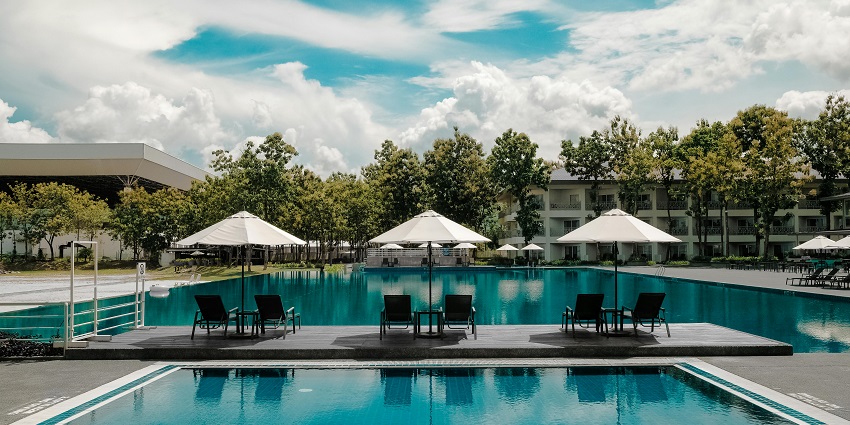 Image of a resort ith swimming pool and lush green tree surrounded under clear blue skky