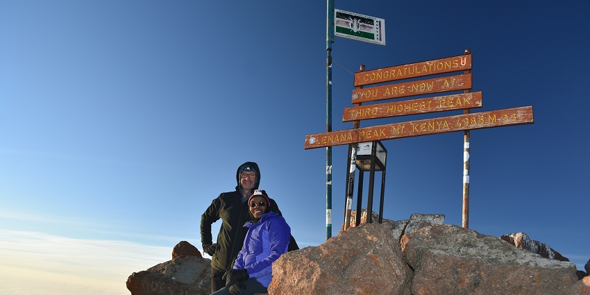 People with bags and their stuff trekking to the peak of Mount Kenya under the blue sky.