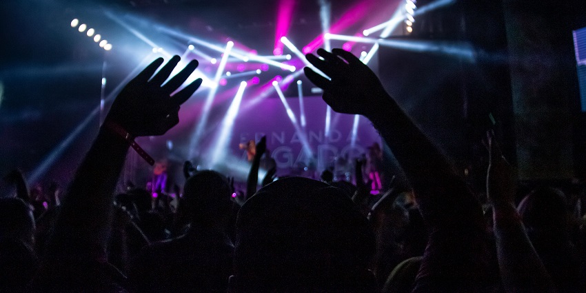 An image of a man playing guitar on stage, surrounded by an energetic nightclub crowd.