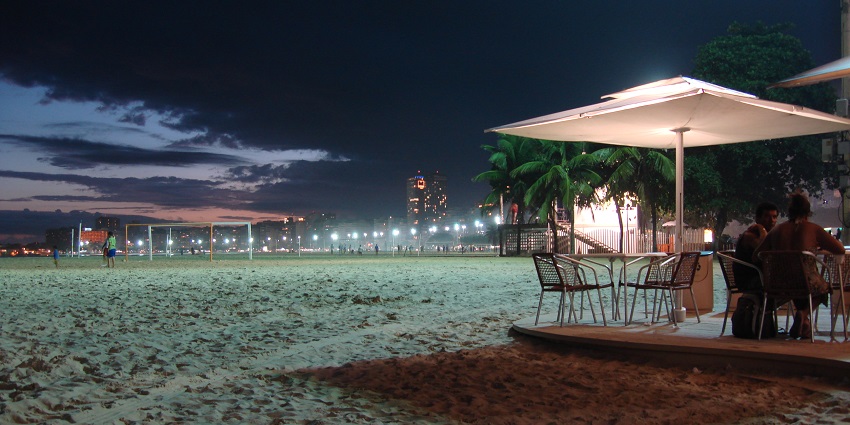 Beach with people sitting in an outdoor dining area and other people walking the area