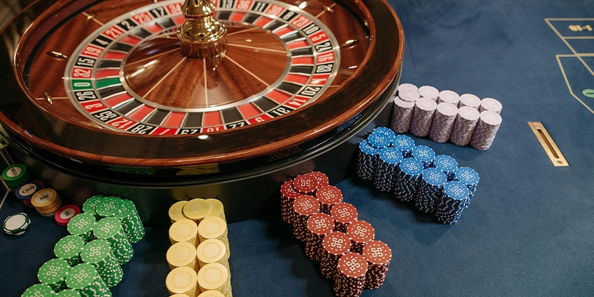 Stacked-up casino poker chips of different colours beside casino roulette on a blue table