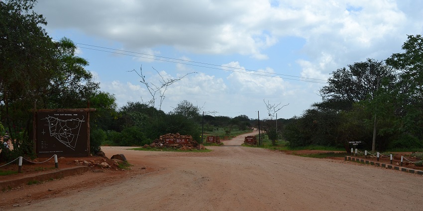 Entrance to the Tsavo East National Park with safari dirt road and a signboard with a map.