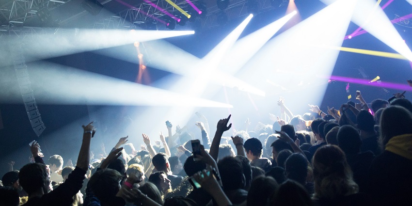 Nightclub setting with a bar, games, people, music, digital posters and neon lights.