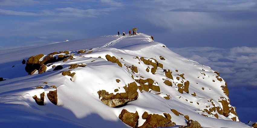 Uhuru Peak of Mount Kilimanjaro covered in snow and people standing on the edge