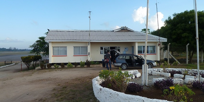 Ukunda Airport showing white building, some plants and people unloading luggage from car