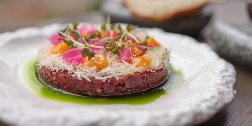 Meat presented on a coconut piece with green leaves on a wooden table under dark light.