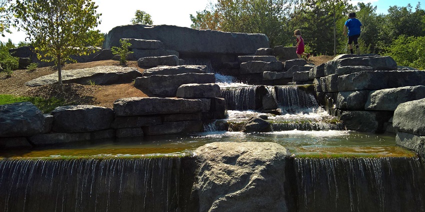 Children playing on a stone fountain next to Lac aux Castors in Mount Royal Park
