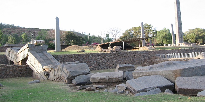 The ancient ruins of Axum in Ethiopia are scattered on the ground covered with grass.