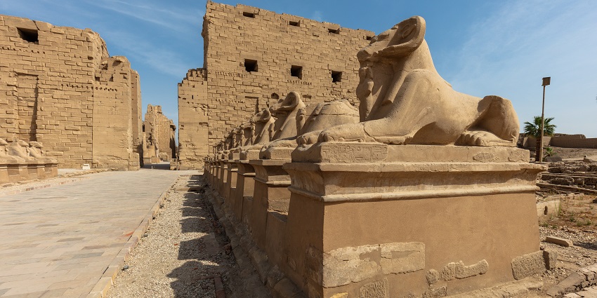 Avenue of sphinxes with multiple intricately detailed statues and ruined structures