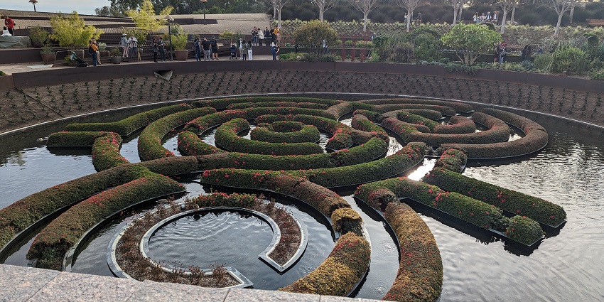 An image of The Getty Center's central garden with a fountain, lush greenery, and clear skies