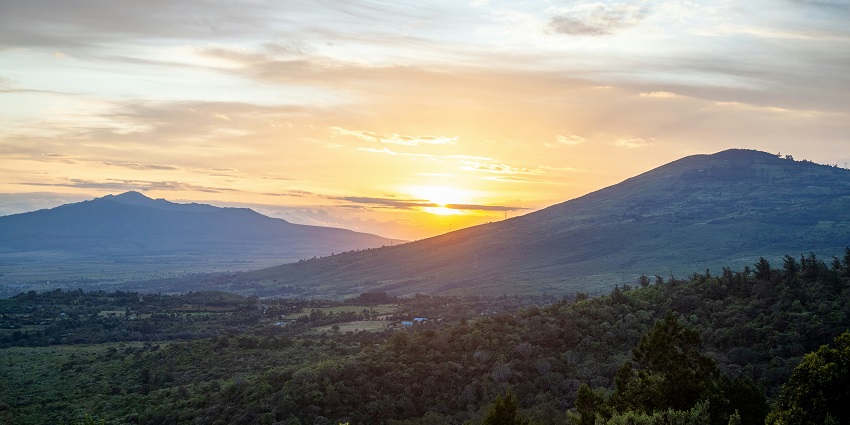Sun is setting between two lofty hills in the Great Rift Valley, covered entirely in green