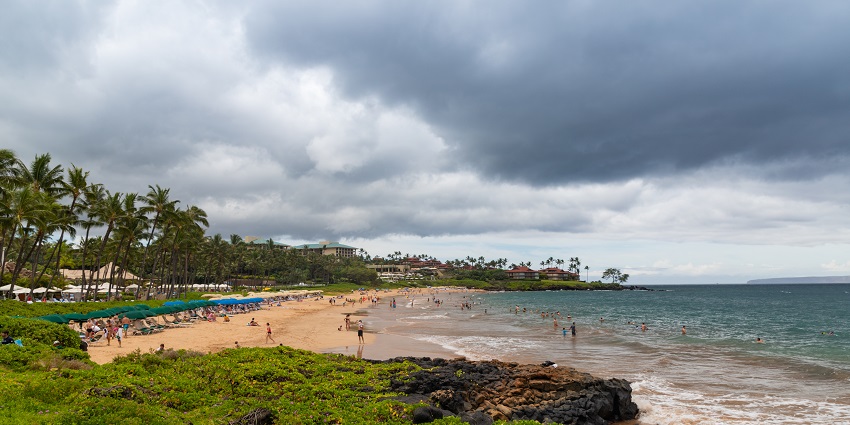 People are enjoying the turquoise water at Wailea Beach, surrounded by lush greenery