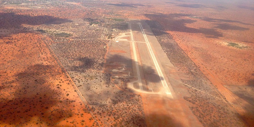 A distant view of the Wajir airport air strip surrounded by barren land, some trees and shadow of clouds
