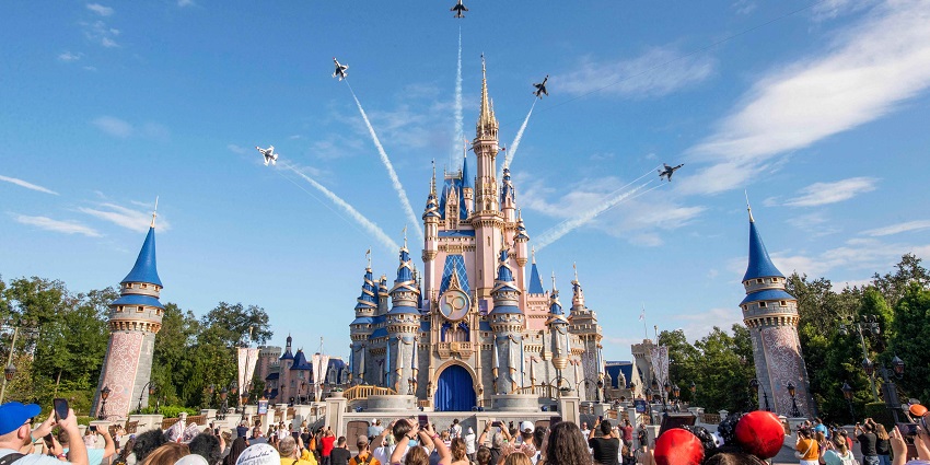 People clicking pictures of the Walt Disney castle and thunderbirds flying over them.