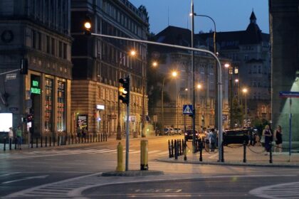 Roads of Warsaw at night with street lamps, people walking in the lanes near the shops.