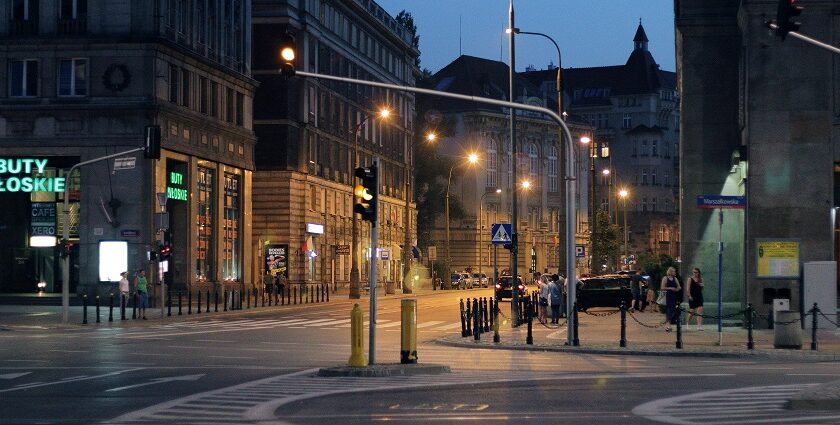 Roads of Warsaw at night with street lamps, people walking in the lanes near the shops.