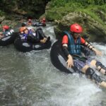 A picture of a group of people enjoying river rafting in a lush green environment.