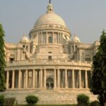 An image of a grand temple in Kolkata having a dull golden dome and lots of people.