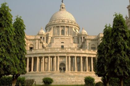 An image of a grand temple in Kolkata having a dull golden dome and lots of people.