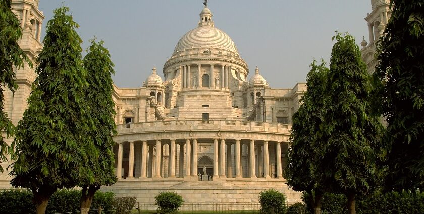 An image of a grand temple in Kolkata having a dull golden dome and lots of people.