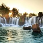 An image of a Wembley waterfall, flowing over the rocks, into a peaceful pool during sunset.