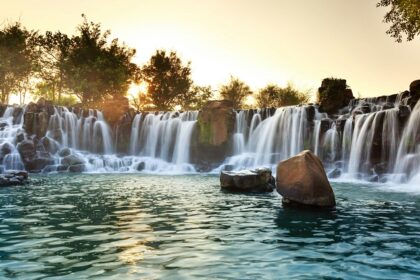 An image of a Wembley waterfall, flowing over the rocks, into a peaceful pool during sunset.