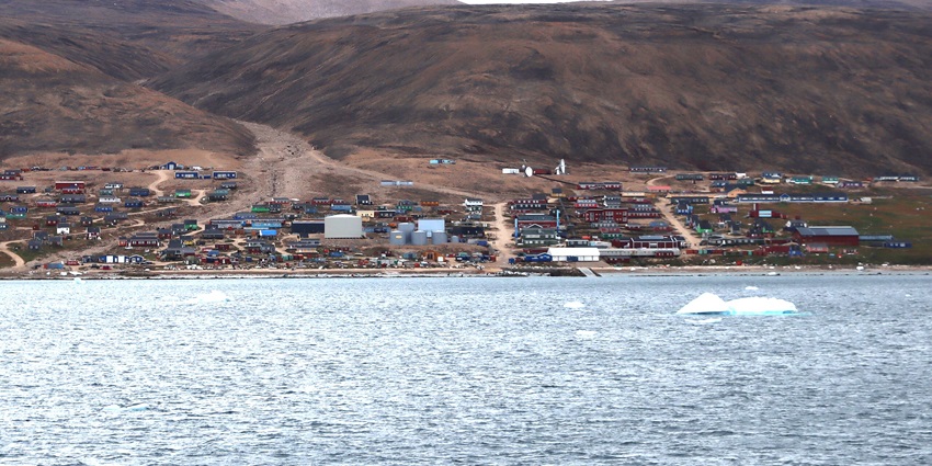 A mesmerising view of Qaanaaq featuring the shimmering blue waters and a village.