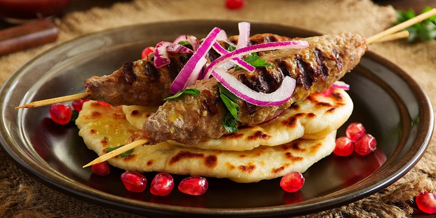 On a platter, there are kebabs placed on bread pieces garnished with pomegranate seeds
