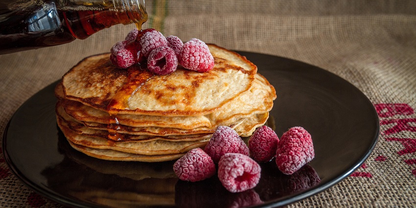 Image of pancakes served on a plate with chocolate syrup and honey on top, also the berries
