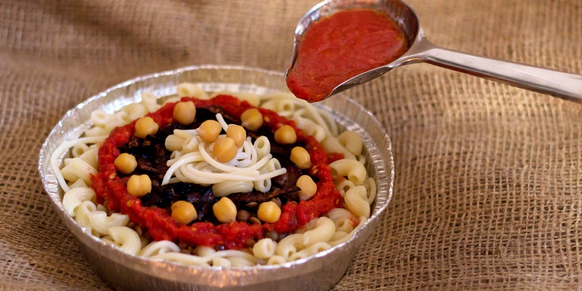 A famous Egyptian dish, Koshari, is served in a bowl with a ladle full of red sauce