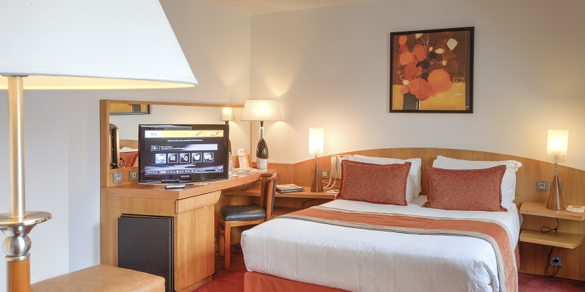 Inner view of a well-lit hotel room which has almost all necessities, such as bed and lamp