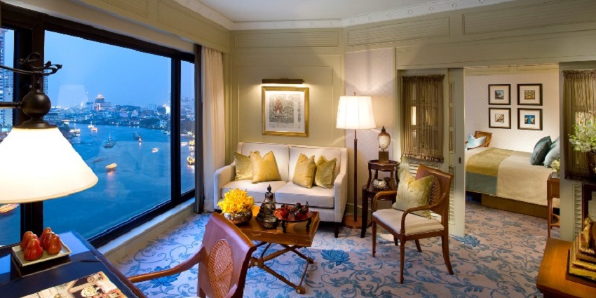 A lavish executive suite room with a view of a river from a glass window.