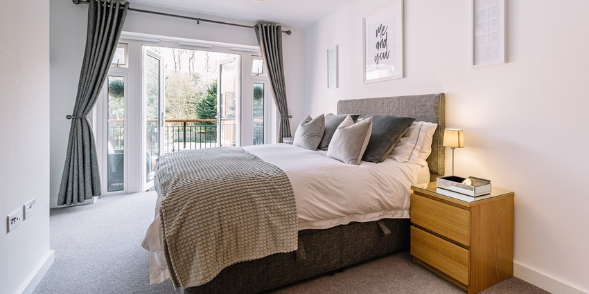 A cosy bedroom with a neatly made bed, decorative pillows, and soft lighting in a modern design.