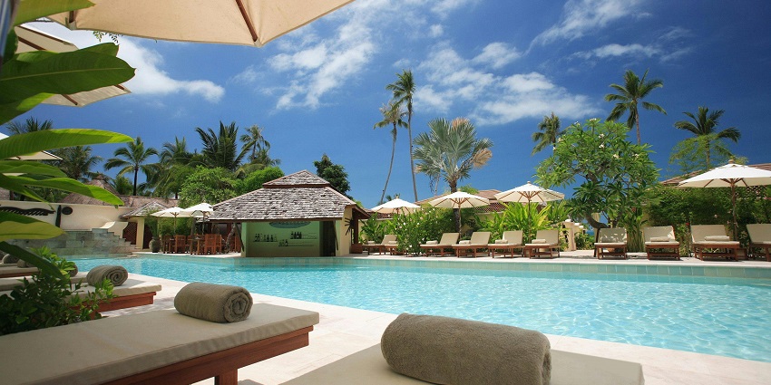 A luxurious resort with a pool and scenic views of beach surrounded by lush greenery