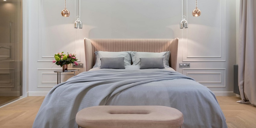 An image showing a cosy bedroom interior with a bed, a table, and hanging lamps above.
