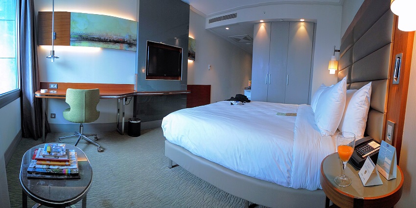 An image of a hotel room with a sof on the side and a TV also a side table with a cosy bed
