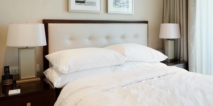 A tidy hotel bedroom with clean pillows and a cozy bed alongside which there is a lamp