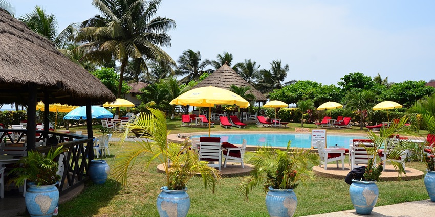A beach resort in Sekondi-Takoradi, Africa showing a pool, chairs, umbrellas and trees around.