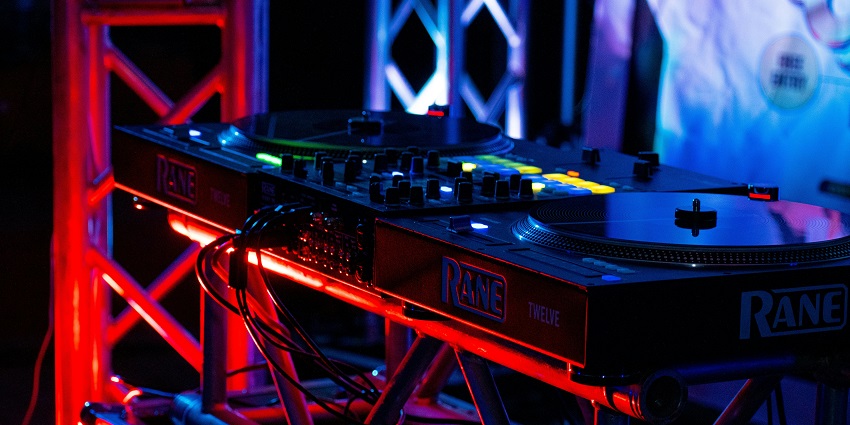 An image of a DJ wearing sunglasses and a hat and performing at a party in a nightclub in Canada.