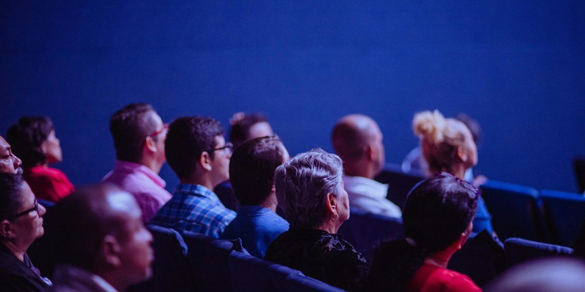 Multiple people sitting on lounge chairs inside of a cinema theatre facing forward