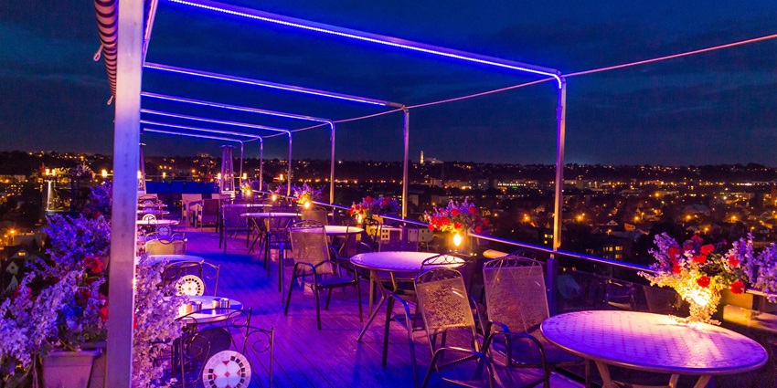 Rooftop restaurant with purple lighting and flower pots on each table with chairs