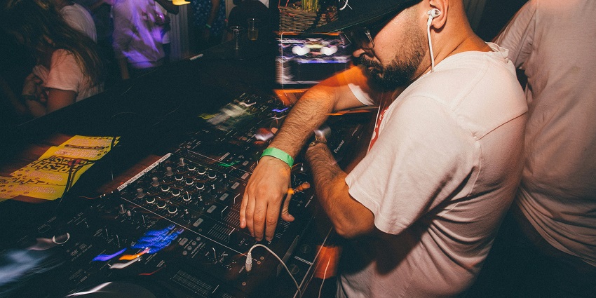 Image of a DJ playing music in a party - disco lights and people vibing with the music