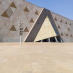 An outer structure of the Grand Egyptian Museum can be seen, covered in triangle glass.