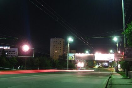 Lit street lamps at the side of the road at night in Chisinau with billboards and buildings