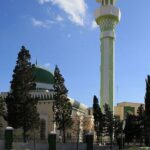 One among the mosques in Malta with a long green and white minaret and a couple of cars parked.