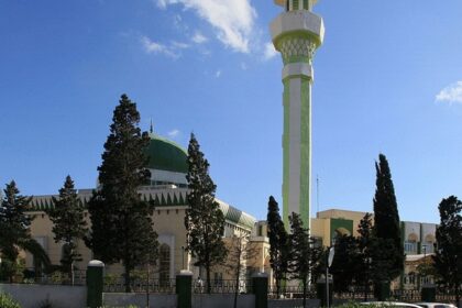 One among the mosques in Malta with a long green and white minaret and a couple of cars parked.