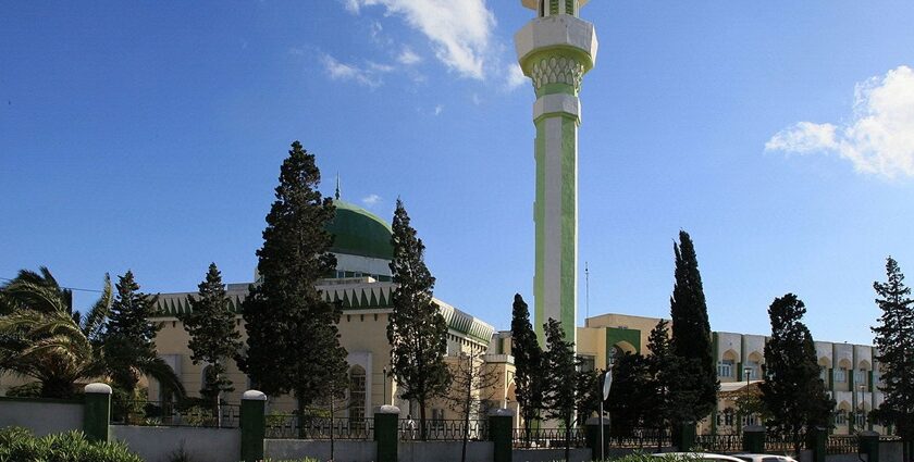 One among the mosques in Malta with a long green and white minaret and a couple of cars parked.