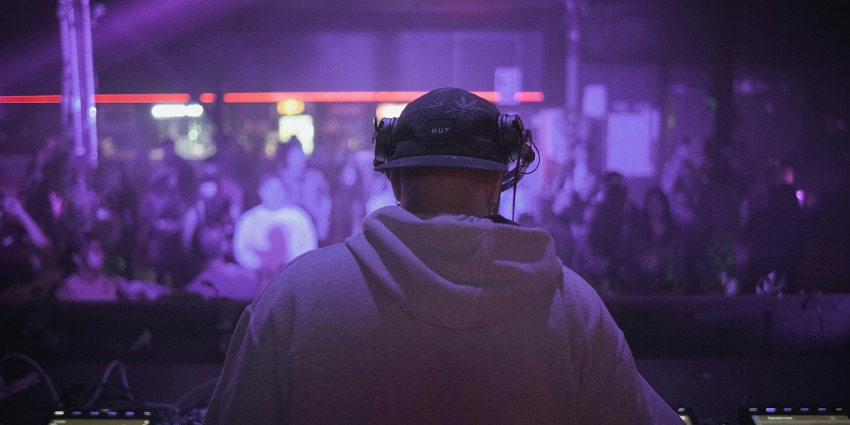DJ performing on stage during a concert in a club, surrounded by an energetic crowd.