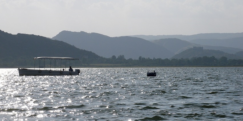 A peaceful view of Pichola Lake, with surrounding trees and hills resembling Ahar Lake